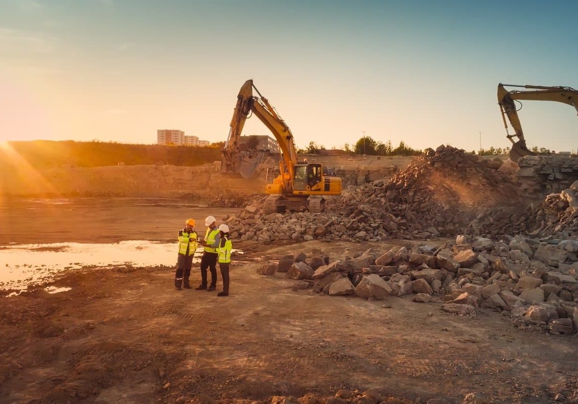 Aerial Drone Shot Of Construction Site With Excavators On Sunny Day: Diverse Team of Real Estate Developers Discussing Project. Civil Engineer, Architect, Inspector Talking And Using Tablet Computer.