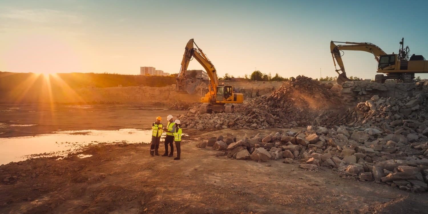 Aerial Drone Shot Of Construction Site With Excavators On Sunny Day: Diverse Team of Real Estate Developers Discussing Project. Civil Engineer, Architect, Inspector Talking And Using Tablet Computer.